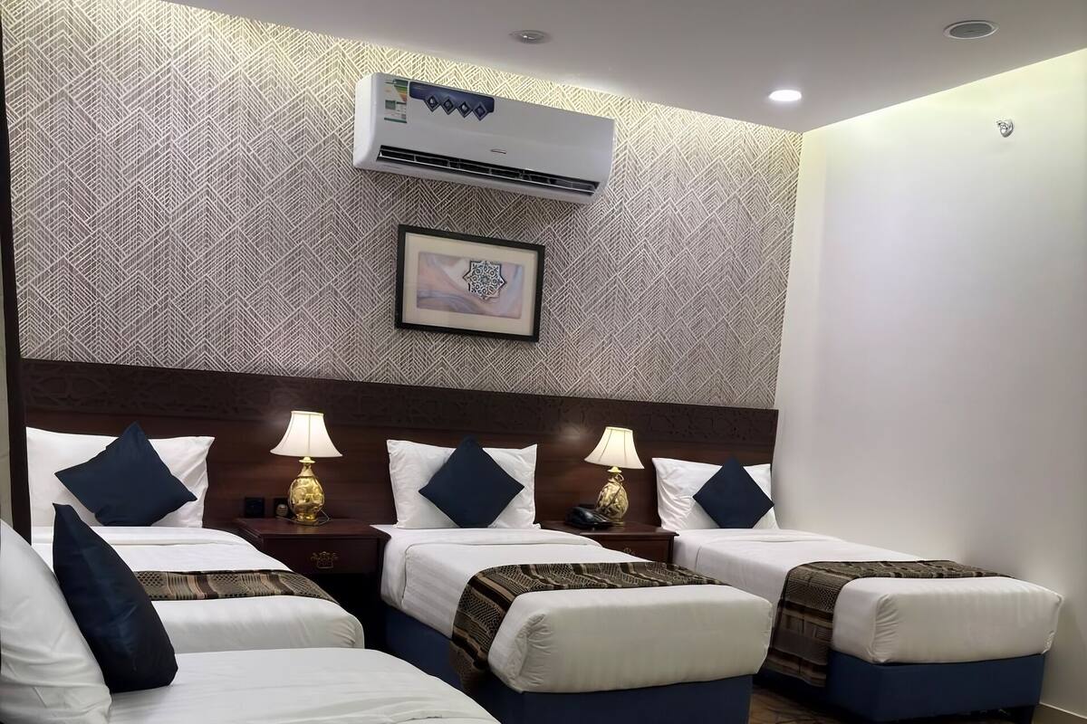 Ein Hotelzimmer mit drei Betten, einer Wand mit Muster, einer Klimaanlage und einem gerahmten Bild.