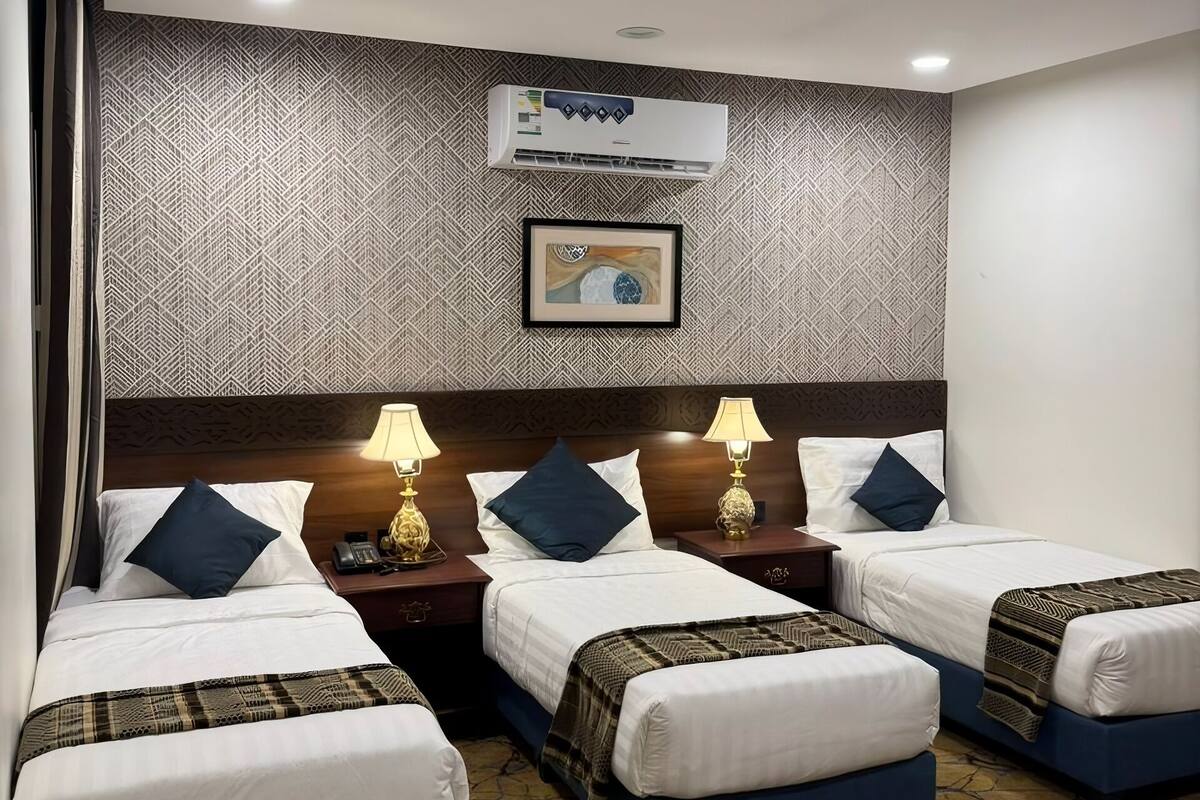 Ein Hotelzimmer mit drei Betten, einer gemusterten Wand, einer Klimaanlage und einem gerahmten Bild.