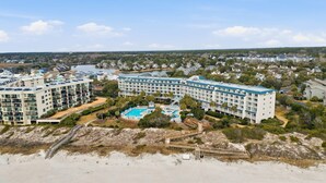 Un hotel frente a la playa con varias edificaciones, una piscina y un acceso peatonal a la playa.