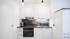 A compact kitchen with white cabinets, a built-in oven, a coffee maker, and a backsplash with a mountain scene. - 2-Schlafzimmer-Apartment mit Bergblick für 4–6 Personen (Alpenresidenz (Bad Gastein))