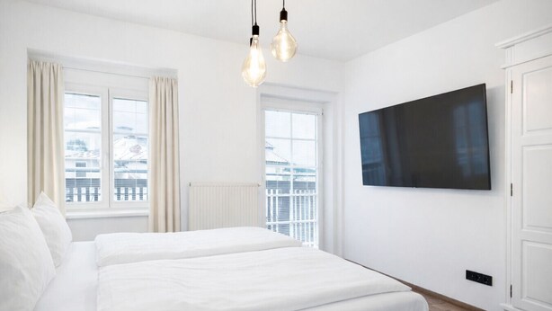 A modern hotel room with a large bed, two windows, a flat-screen TV, and a wardrobe. - 2-Schlafzimmer-Apartment mit Bergblick für 4–6 Personen (Alpenresidenz (Bad Gastein))