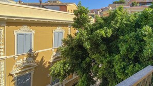 Un edificio amarillo con contraventanas azules, detalles arquitectónicos ornamentales y un árbol en primer plano.