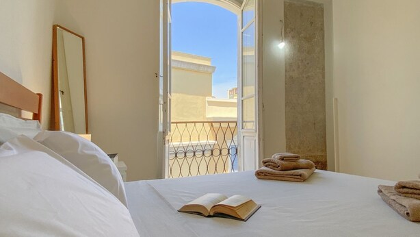 Habitación de hotel con cama, puerta abierta a un balcón y un libro sobre la cama.