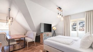 A modern bedroom with a wooden floor, a bed, a desk, a chair, a TV, and a lamp. - Deluxe Apartment mit 57 m² für 2–4 Personen (Alpenresidenz (Bad Gastein))