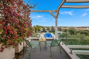 Ein Balkon mit Blick auf einen Swimmingpool, grüne Stühle und ein Tisch mit Flasche und Gläsern.