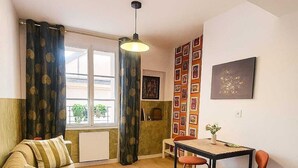 Un espace de vie compact comprenant un canapé, une table à manger avec des chaises, une cheminée et un mur décoré de tableaux encadrés.