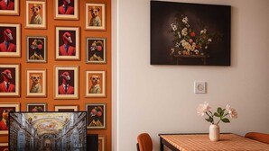 Une pièce dont un mur est décoré d’œuvres d’art encadrées, avec un téléviseur à écran plat, une table ornée d’un vase de fleurs et une chaise.