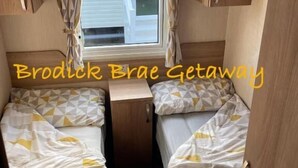 Interni di un camper compatto con due letti, un tavolino e una finestra con tende.