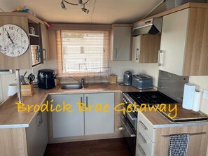 A compact kitchen with a stove, sink, and various appliances. - Brodick Brae Getaway (Ayr)