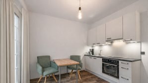 Una cocina compacta con una mesa de madera y dos sillas, horno integrado y armarios blancos.