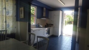Cocina pequeña con armarios blancos, estufa y tostadora. Hay una mesa de comedor con sillas y una ventana que proporciona luz natural.