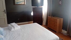 Un dormitorio con cama, cómoda, televisor y un cuadro en la pared.