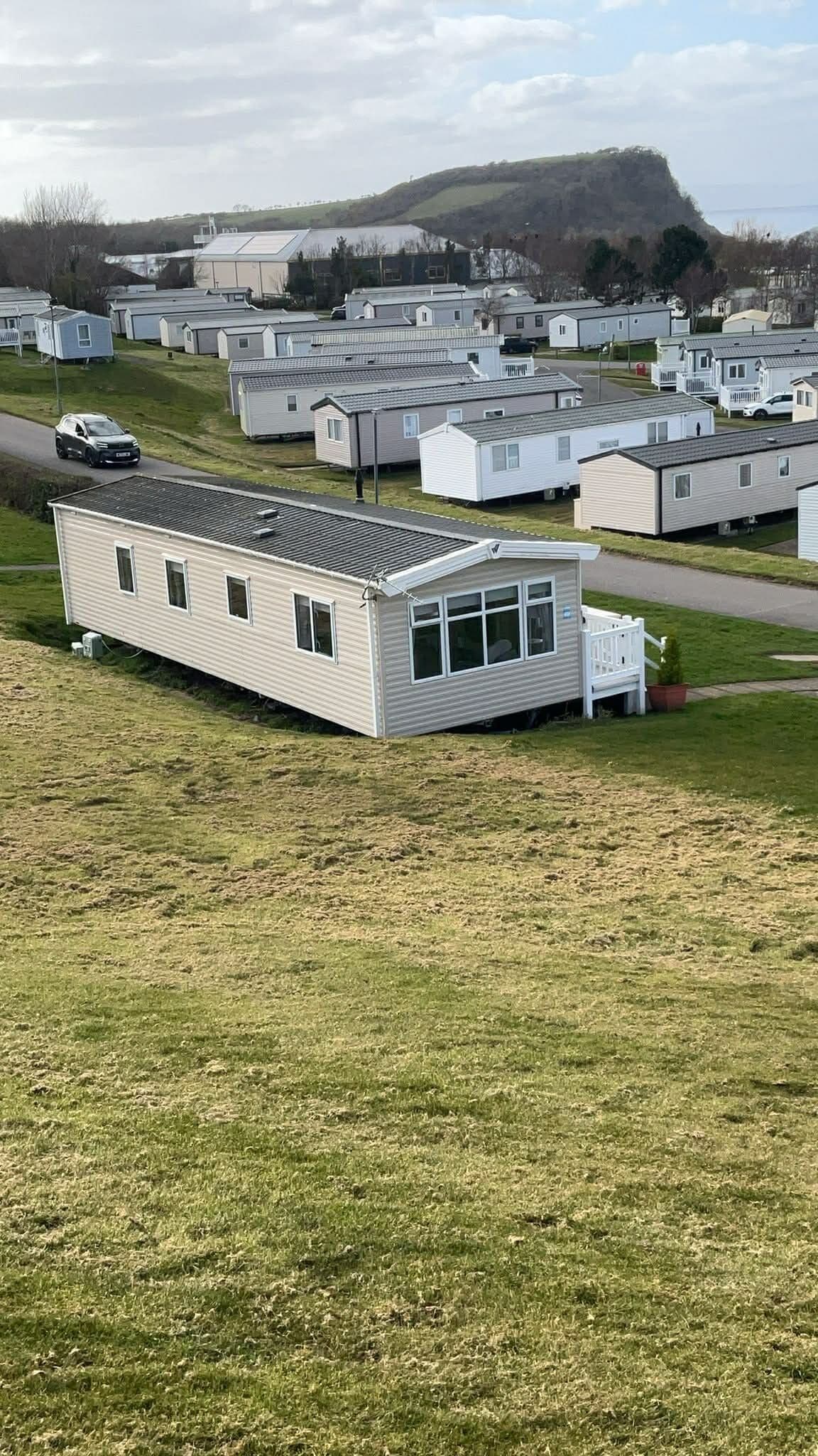 A row of mobile homes with a grassy field in the foreground and a hill in the background.