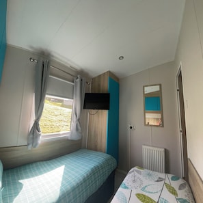 Een slaapkamer met een bed, een raam met gordijnen, een bevestigde televisie, een radiator en een spiegel aan de muur.