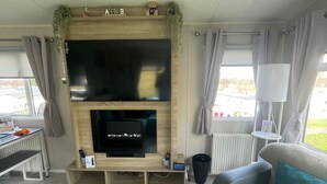 Un salon moderne doté d’un téléviseur à écran plat, d’un meuble de rangement en bois, d’un canapé gris et offrant une vue sur l’extérieur.