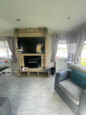 Een moderne woonkamer met een flatscreen televisie, een houten tv-meubel, een grijze bank en uitzicht op de omgeving.