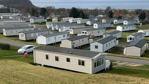 Une rangée de maisons mobiles, avec un champ verdoyant au premier plan et une étendue d’eau en arrière-plan.