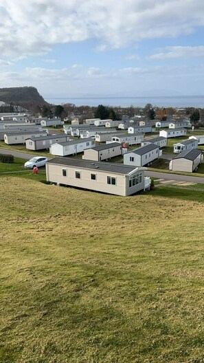 Een rij mobiele woningen met een grasveld op de voorgrond en een waterpartij op de achtergrond.
