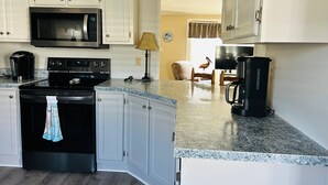 Una cucina con mobili bianchi, un forno a microonde, un piano cottura e una macchina per il caffè.