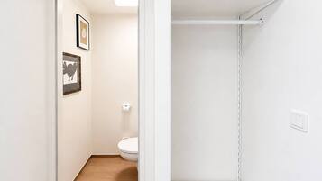 Une salle de bain avec des toilettes, un tableau encadré au mur et une étagère blanche.