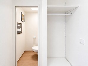 Une salle de bain avec des toilettes, un tableau encadré au mur et une étagère blanche.