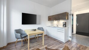A modern kitchen with white cabinets, a wooden countertop, and a coffee machine. There is a dining area with a wooden table and two chairs. - 28 m² Studio mit Balkon für 2 Personen (Alpenresidenz (Bad Gastein))