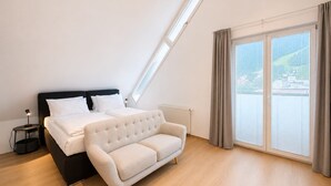 Une chambre à coucher avec un lit, un canapé, une table de chevet, une lampe, une fenêtre avec des rideaux et une vue sur l’extérieur.
