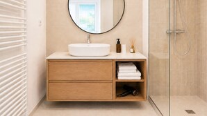 Une salle de bain moderne avec un miroir rond, un lavabo blanc et une douche à parois de verre.