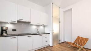 A modern kitchen with white cabinets, a black countertop, and a coffee machine. There is a wooden floor and a wicker chair in the corner. - 55 m² Apartment mit 2 Schlafzimmern für 4 Personen (Alpenresidenz (Bad Gastein))