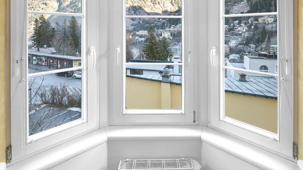 A corner room with three windows overlooking a mountainous landscape and a town below. - 55 m² Apartment mit 2 Schlafzimmern für 4 Personen (Alpenresidenz (Bad Gastein))