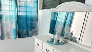 Ein Badezimmer mit weißem Waschtisch, einem Spiegel und einem Fenster mit blauen Vorhängen.