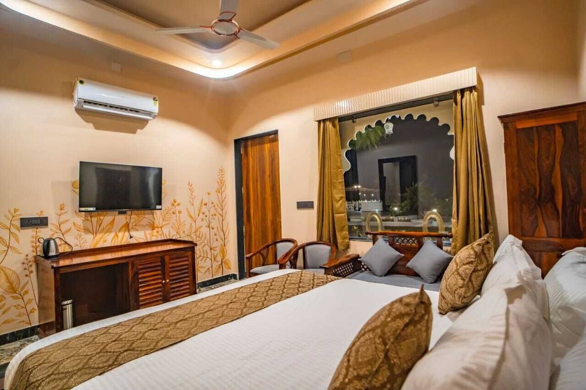 A hotel room with a bed, a TV, a desk, and a window with curtains.