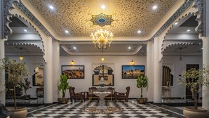 Un vestíbulo con piso de tablones, techo ornamentado, candelabros y plantas en macetas.