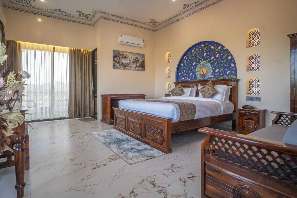 A bedroom with a large bed, a wooden nightstand, a desk, and a decorative wall piece.