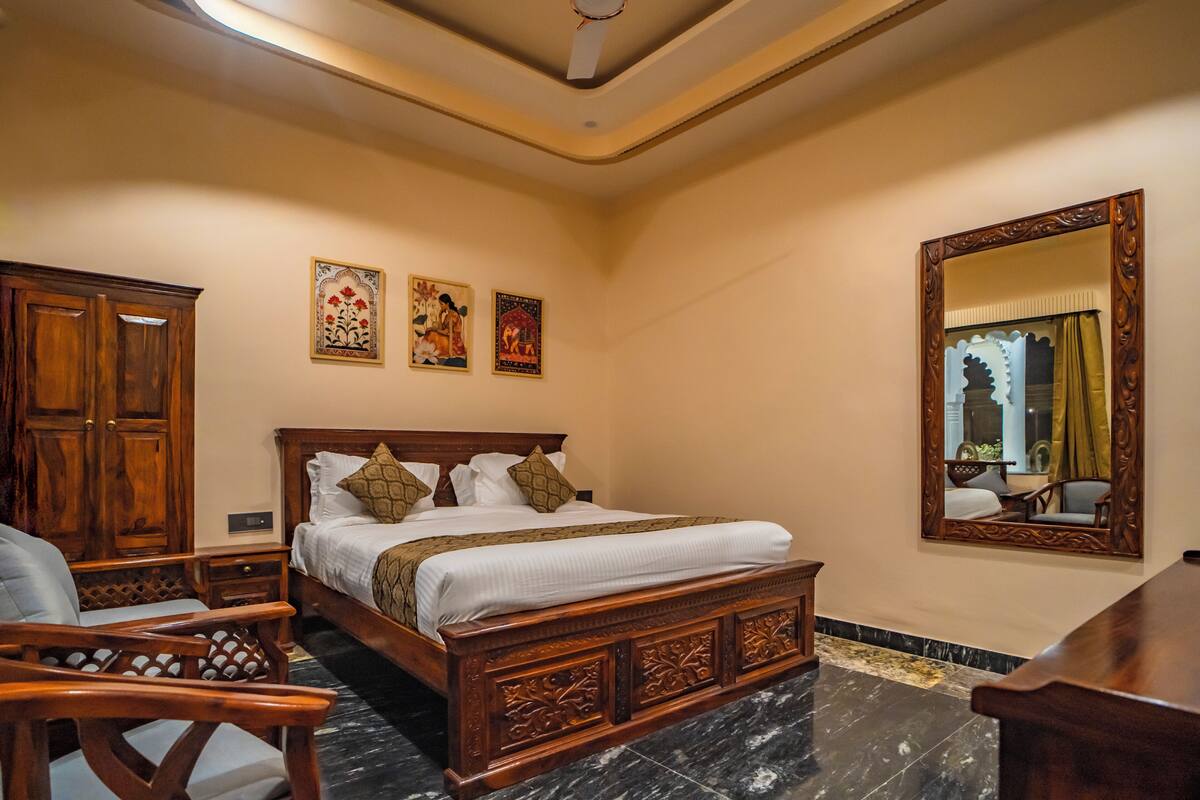 A bedroom with a wooden bed, a nightstand, a chair, a large mirror, and artwork on the wall.