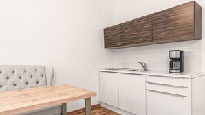 Moderni keittiö, jossa on valkoiset kaapit, puinen ruokapöytä ja kuviollinen sohva.