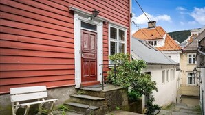 A narrow stone pathway leading to a red wooden house with a white door and steps. - The Red House - Affordable living (Bergen)