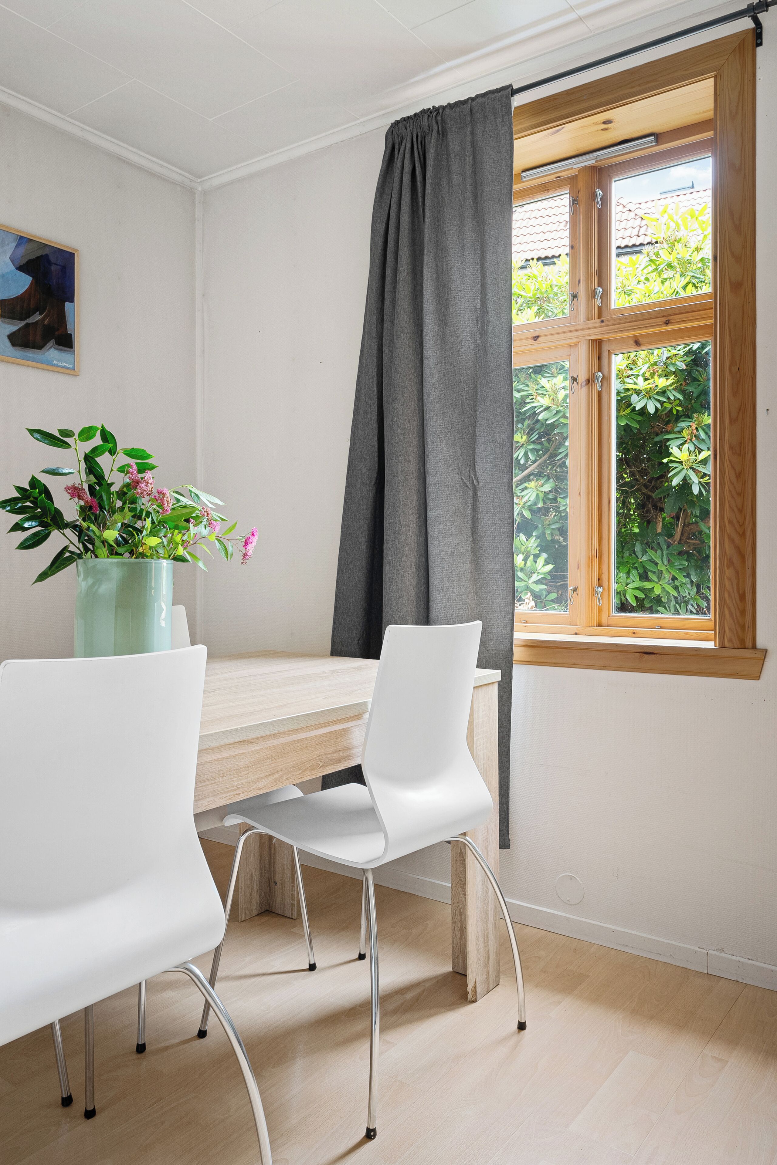 Una habitación con una mesa de comedor, dos sillas blancas, una planta en maceta y una ventana con cortina.
