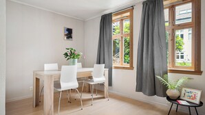 A room with a wooden dining table, white chairs, a potted plant, and a framed picture on a small table. - The Red House - Affordable living (Bergen)