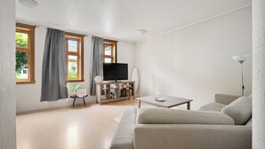 A modern living room with a sofa, a coffee table, a TV on a stand, and a bookshelf. - The Red House - Affordable living (Bergen)
