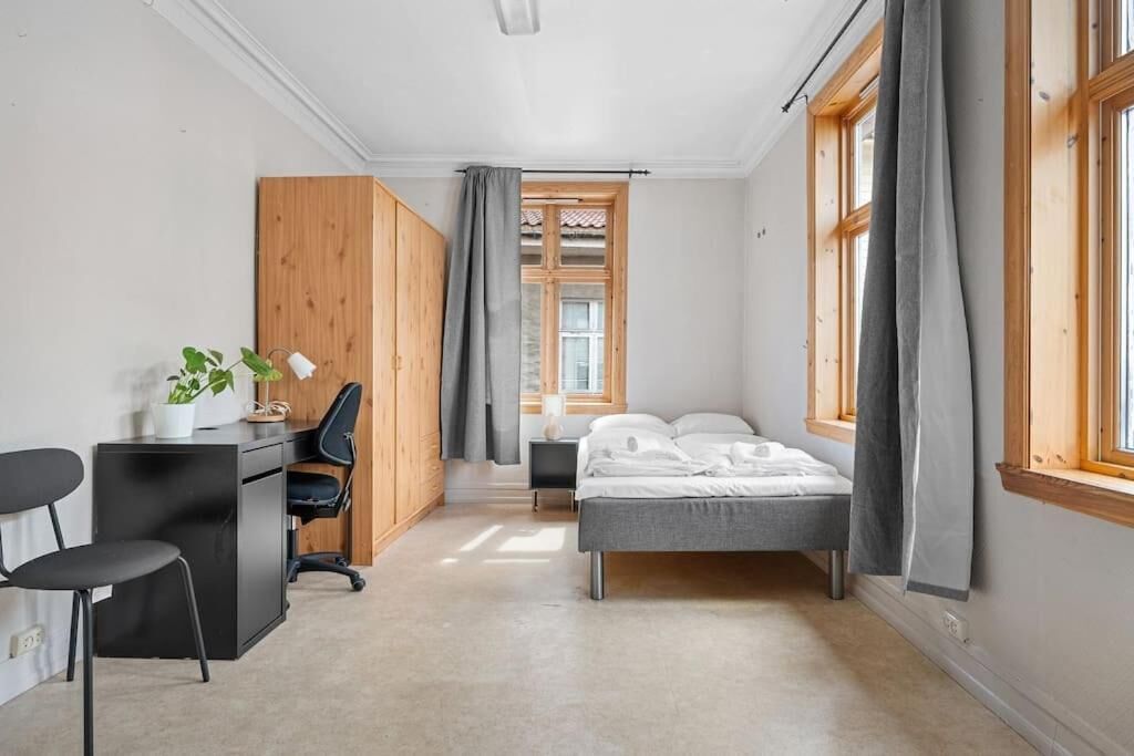 Una habitación compacta con cama, escritorio, silla y una mesita con una planta.