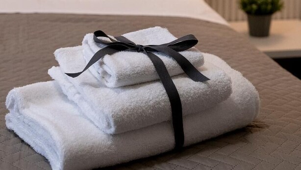 A neatly made bed with white linens and a black ribbon, a wall with a geometric pattern, and a wall-mounted light fixture. - Economy Room from 1 to 3 persons (Roma)