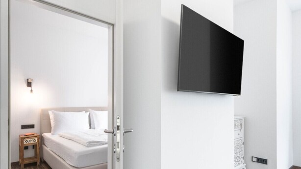 Une chambre d’hôtel moderne, équipée d’un lit, d’une table de chevet, d’un téléviseur fixé au mur et d’un plancher en bois.