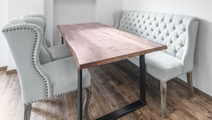 Une pièce comprenant une table en bois, deux fauteuils rembourrés, un banc capitonné, une fenêtre donnant sur un paysage verdoyant et un luminaire suspendu.