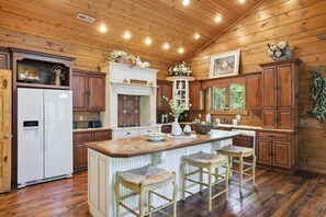 A kitchen with wooden cabinets, a white refrigerator, a central island with bar stools, and a hanging plant. - Timberstone 4 Bedroom Home (Sevierville)