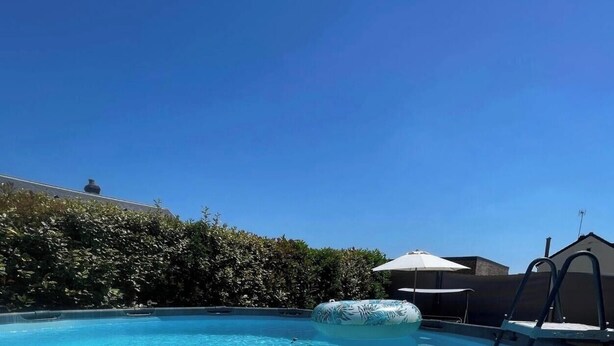 A swimming pool with a lounge chair and umbrella, surrounded by greenery and a building. - Exclusive getaway with pool and jacuzzi (Clermont)