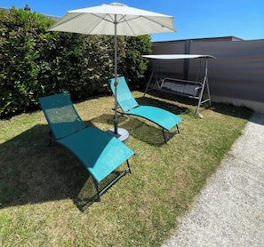 Eine Terrasse mit zwei grünen Liegestühlen, einem weißen Sonnenschirm und einer Schaukel.