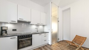 Moderni keittiö, jossa on valkoiset kaapit, sisäänrakennettu uuni ja kahvinkeitin.