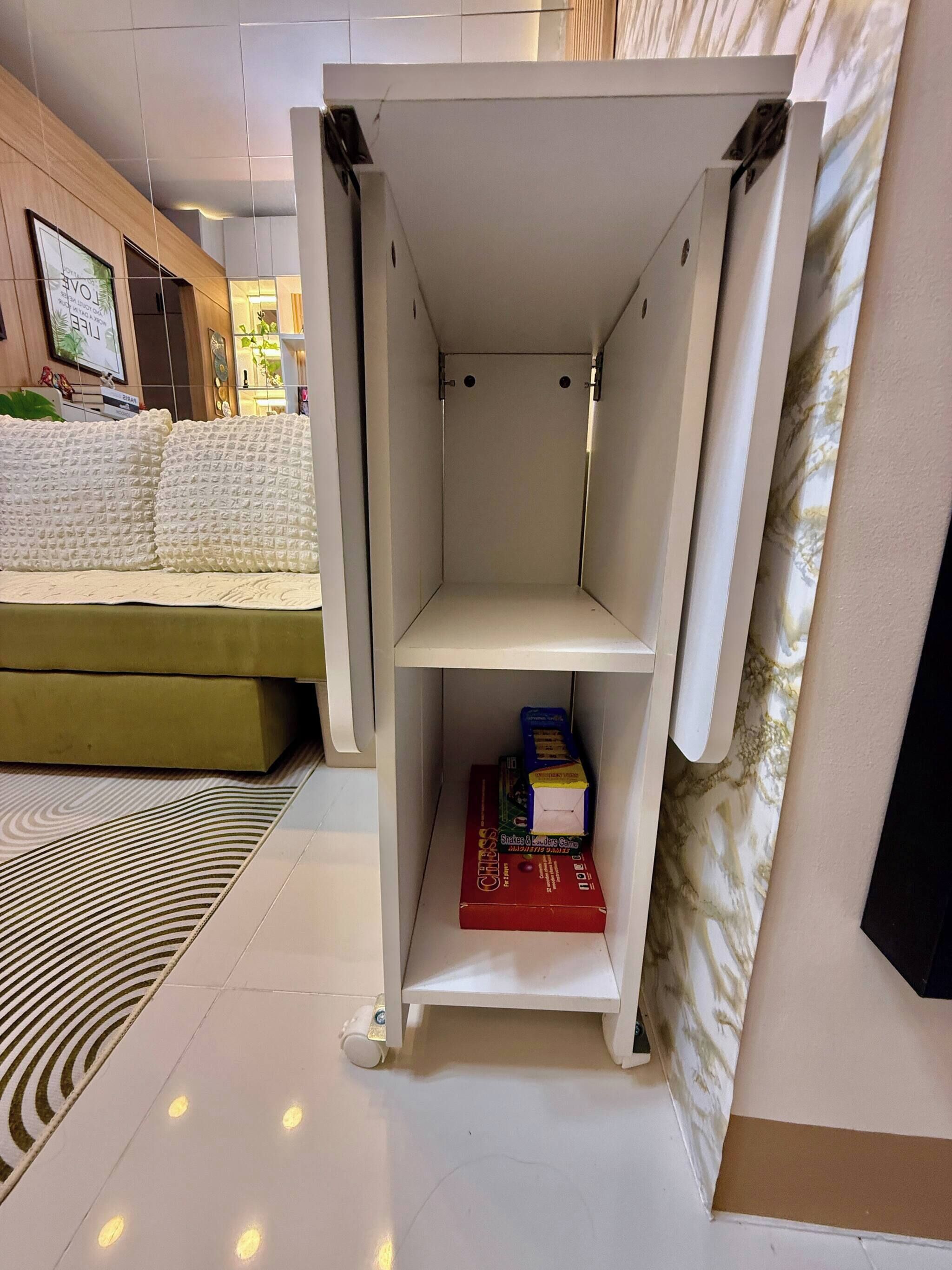 Une étagère blanche à deux niveaux ouverts, un canapé vert et un tapis à motifs dans une pièce au style moderne.