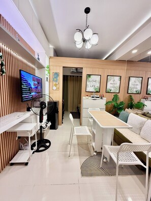 A modern living room with a flat-screen TV, a ceiling fan, a dining area with a table and chairs, and a sofa. - MJM Cityscape At Red Residences Makati (Makati)